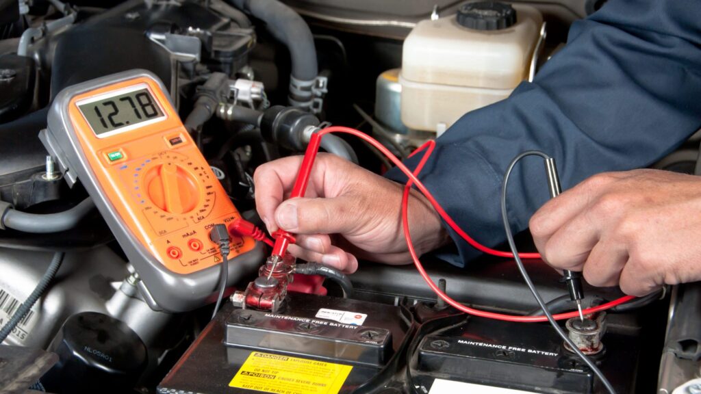 Technician testing a truck battery with a digital multimeter under the hood.