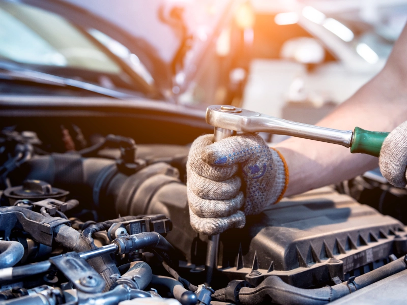 Mechanic working on car engine with tools in hand.
