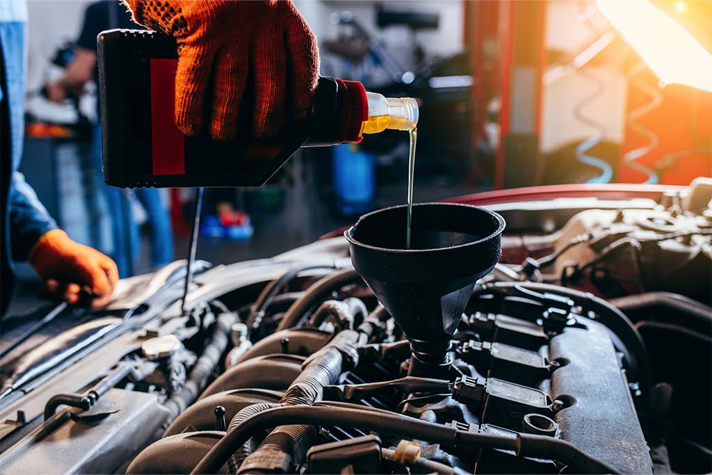 Technician pouring engine oil into a truck engine during maintenance.