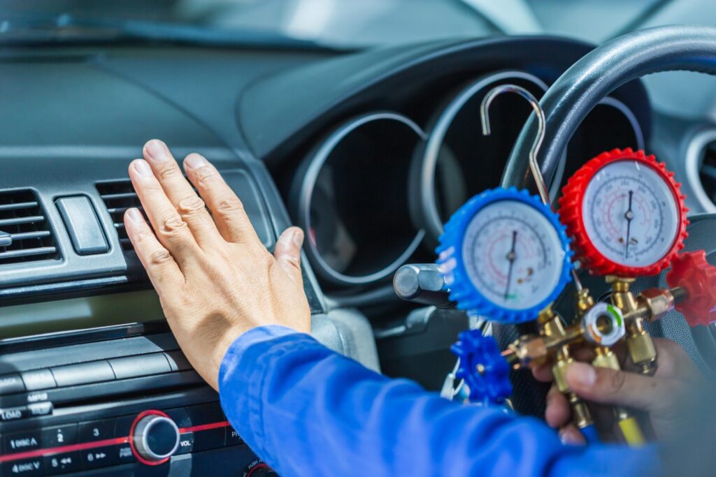Technician checking truck air conditioning system with gauges inside vehicle.