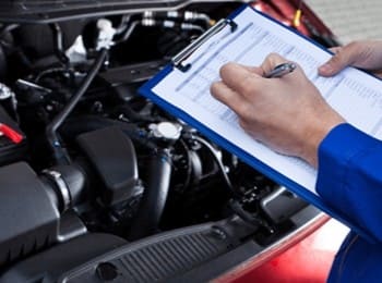 Technician inspecting car engine during service at Mazda Pros Inc.