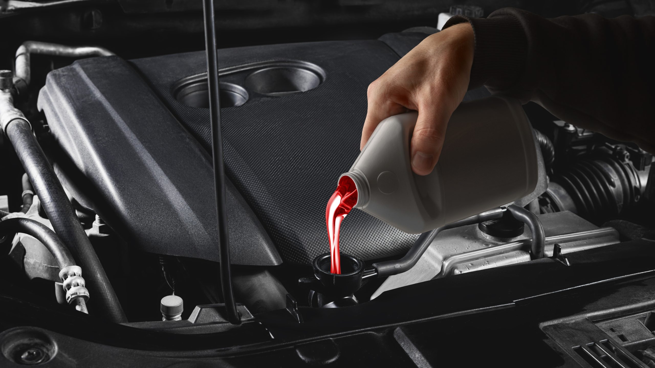 Person pouring transmission fluid into Mazda engine for maintenance.