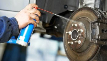 Technician inspecting vehicle brake system with spray can in auto repair shop.