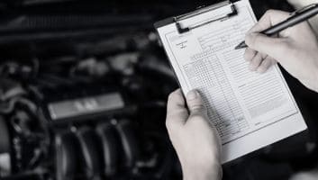 Technician inspecting vehicle engine with clipboard at Meineke Fresno.
