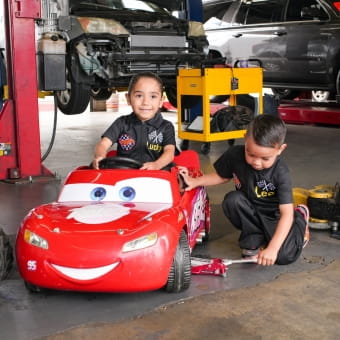 Children playing with a red cartoon-style toy car in an auto repair shop.