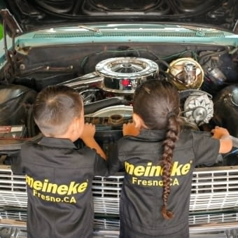 Two kids inspecting a car engine at Meineke Car Care Center.