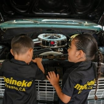 Two technicians inspecting a car engine at Meineke Fresno.
