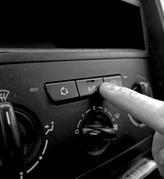 Person pressing A/C button on car's climate control panel.