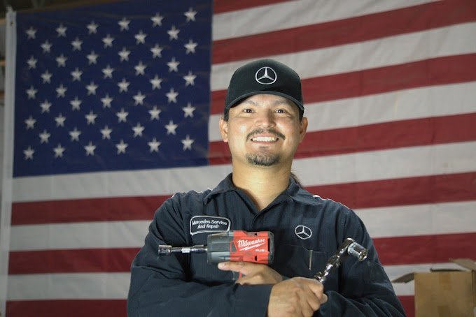 Skilled Mercedes-Benz mechanic holding tools in front of American flag.
