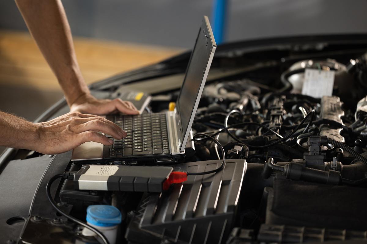 Auto diagnostics being performed on a vehicle engine with a laptop and scanner.