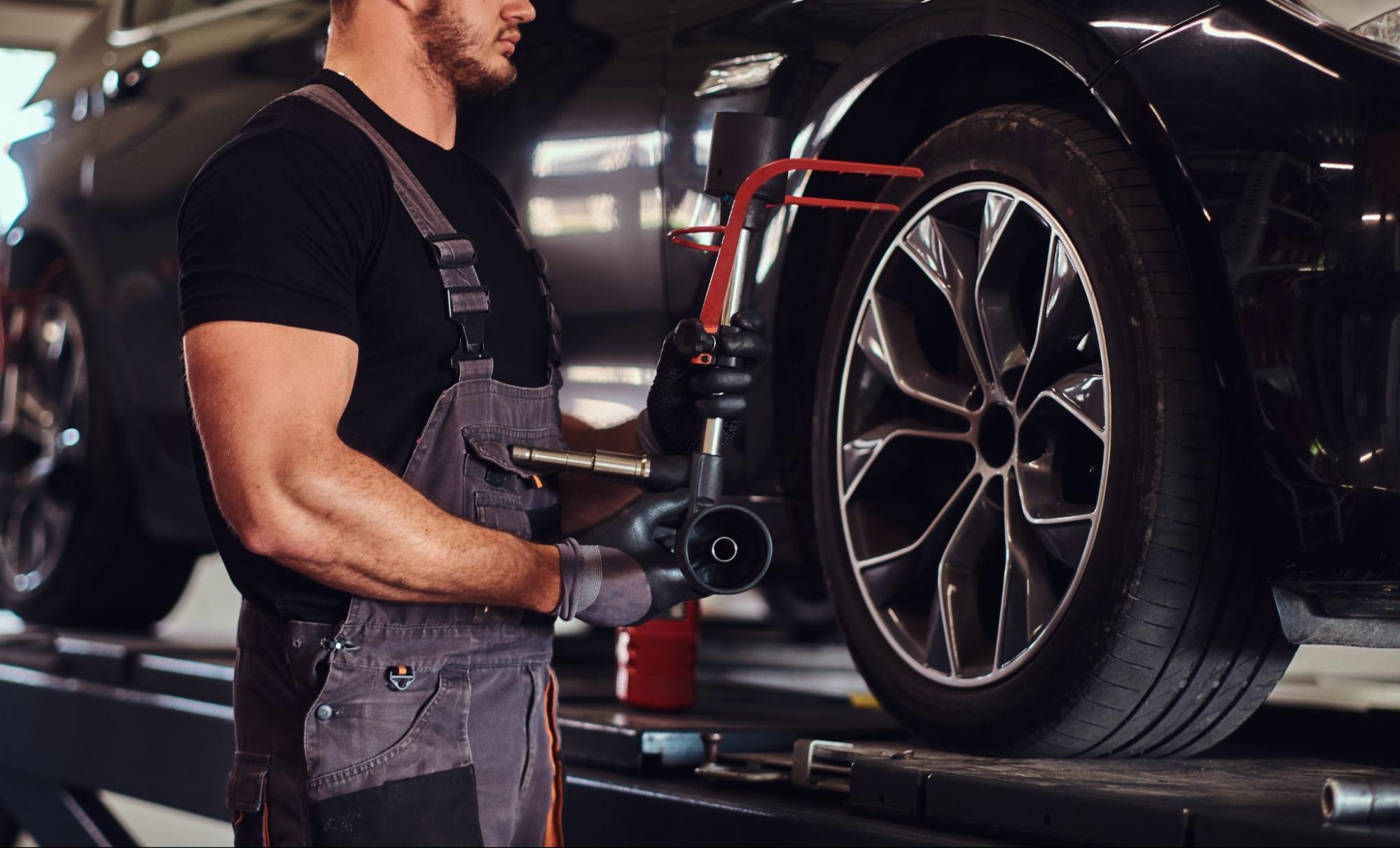 Technician inspecting car wheel alignment to prevent uneven tire wear.