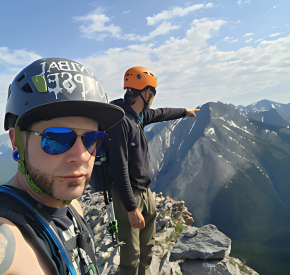 Mountain climbers on a rocky peak with mountain range in background.