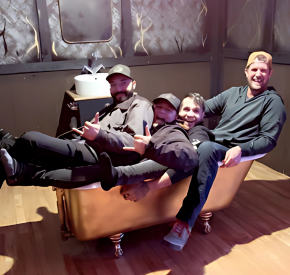 Group of four smiling men relaxing in a vintage bathtub in a modern office space.