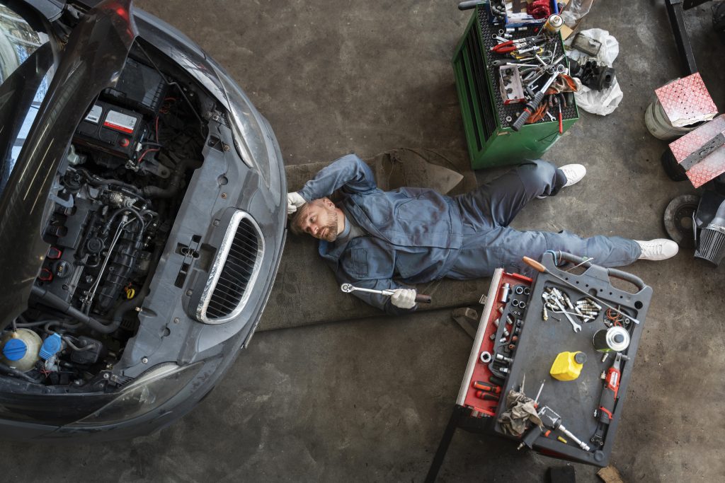 Engine repair technician inspecting a car engine in an auto repair shop.