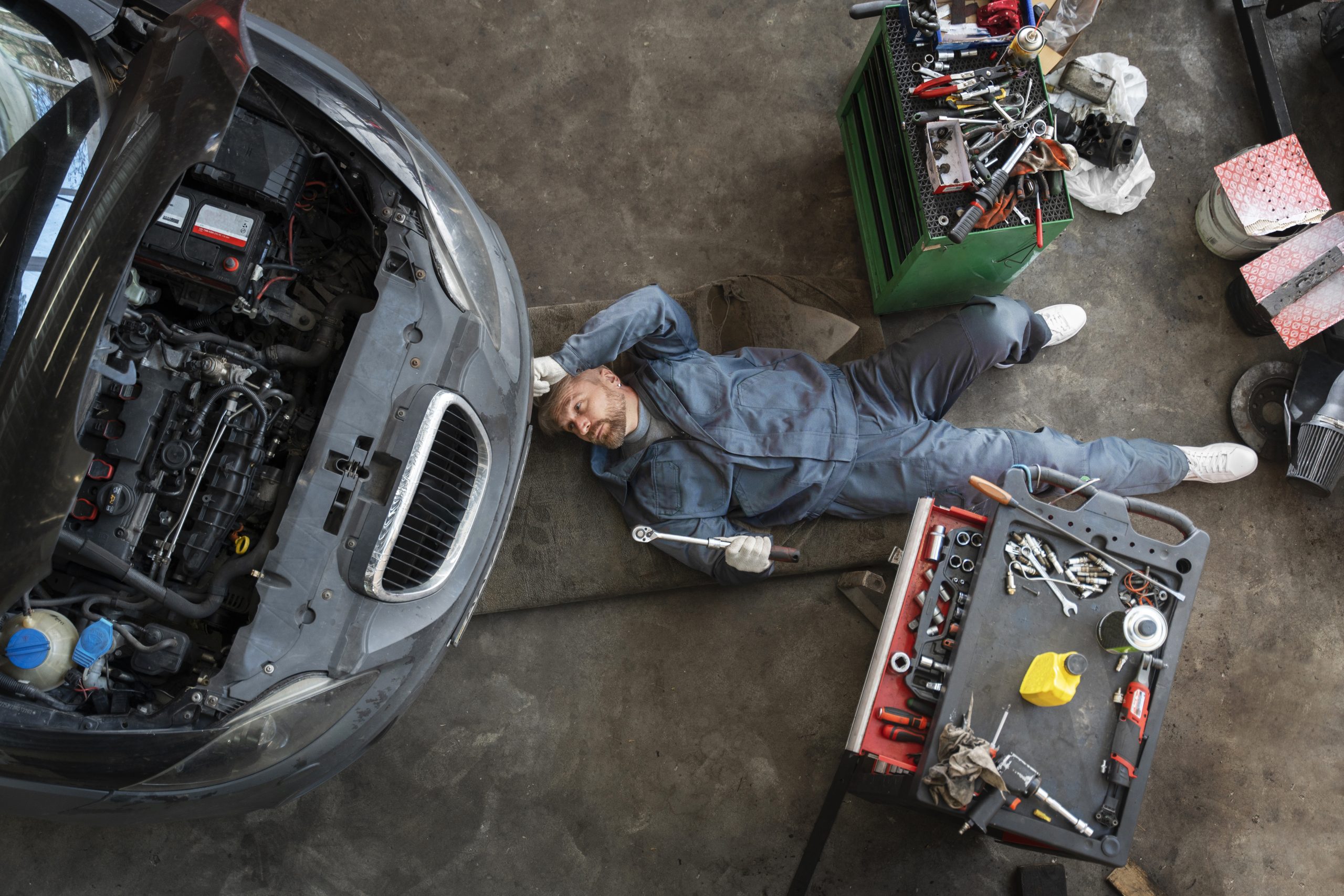 Engine repair technician inspecting a car engine in an auto repair shop.