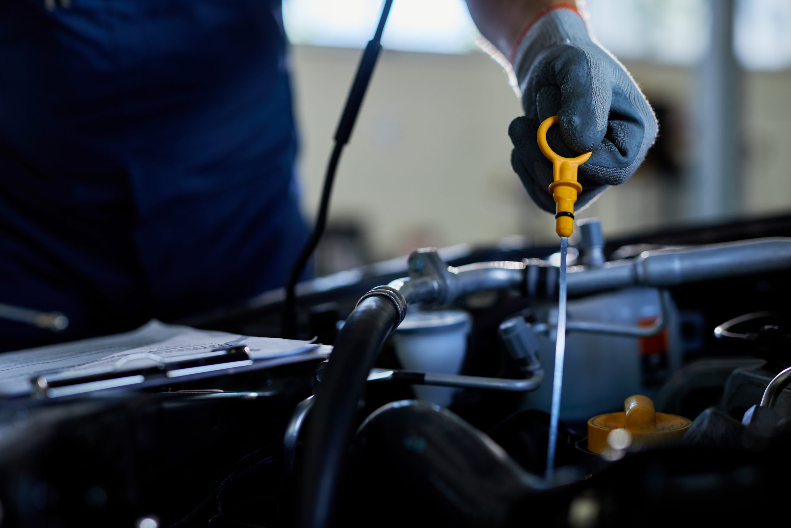 Technician performing engine oil check with dipstick in a professional auto repair shop.