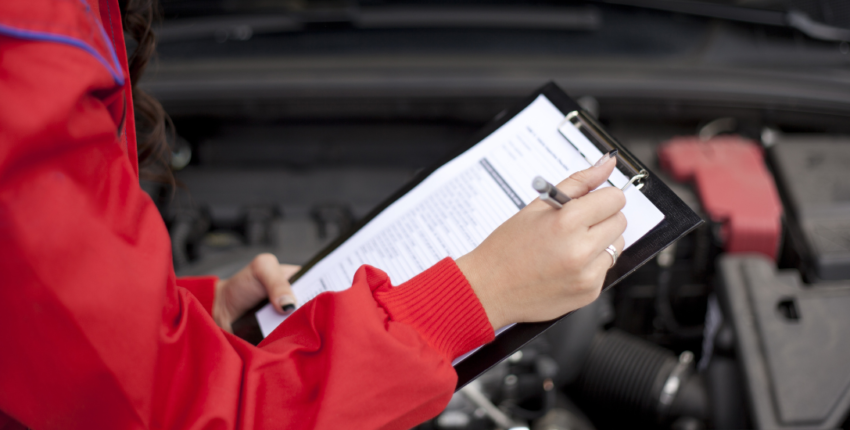 Technician inspecting vehicle engine with clipboard at MJZ Garage auto repair shop.