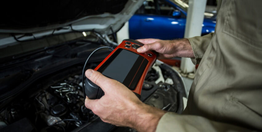 Technician using diagnostic scanner on car engine at MJZ Garage auto repair shop.