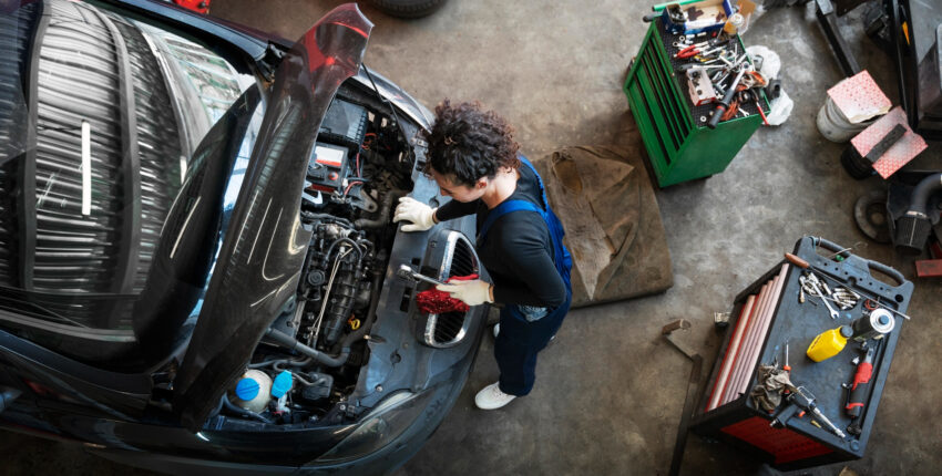 Auto mechanic working on a car engine in a garage setting.