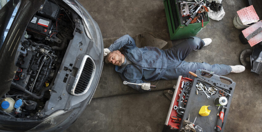 Auto mechanic inspecting car engine in garage workshop.
