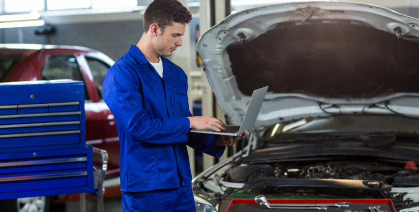 Auto mechanic checking engine in a garage with open hood and tools.