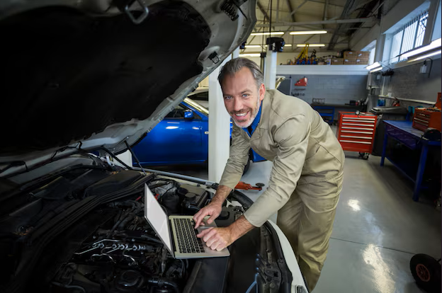 Auto mechanic using laptop for diagnostics under open car hood at MJZ Garage.