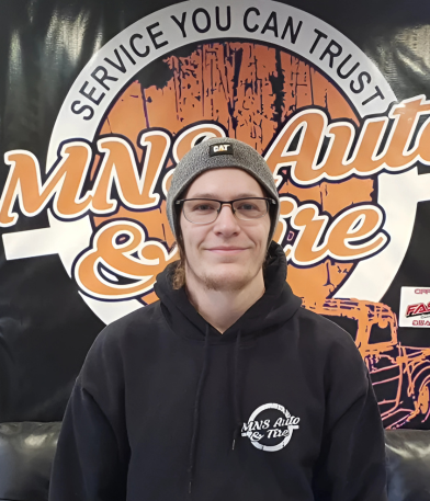 Friendly technician at MNS Auto Services in front of company banner.