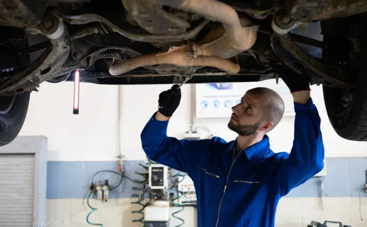 Auto mechanic inspecting underside of vehicle in garage.