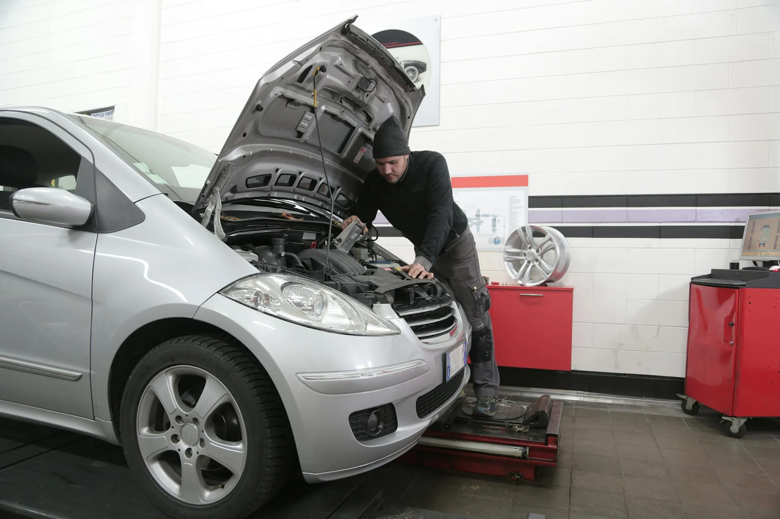 Technician performing oil change on a silver car in auto repair shop.