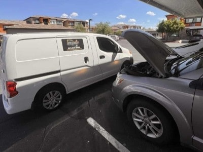 Auto repair technician inspecting a vehicle with open hood at a service center.