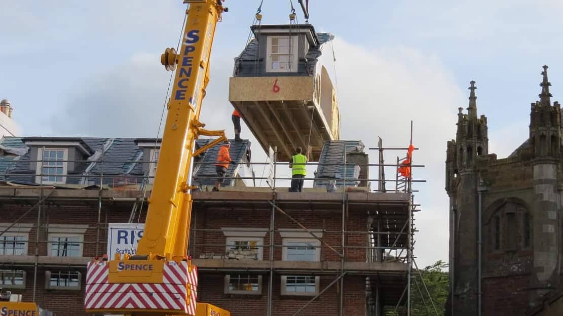 Construction workers install a modular extension on a historic building in progress.