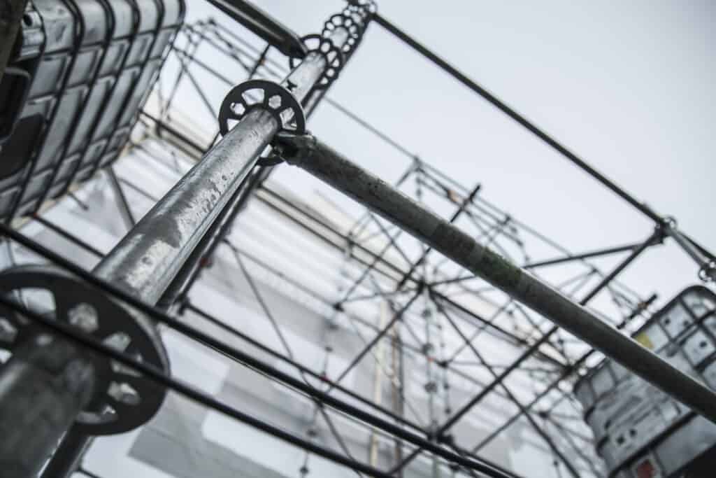 Close-up view of a construction scaffold, showcasing the intricate metal framework and connections, with a background of a building under construction covered in protective sheeting. Essential scaffold safety tips, common pitfalls, and expert advice are crucial for securing your construction site effectivel