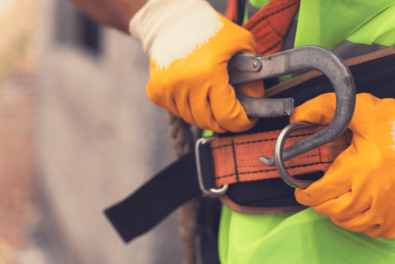Worker wearing safety harness and gloves securing lanyard for work at height training.
