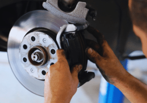 Technician inspecting brake caliper on vehicle wheel assembly.