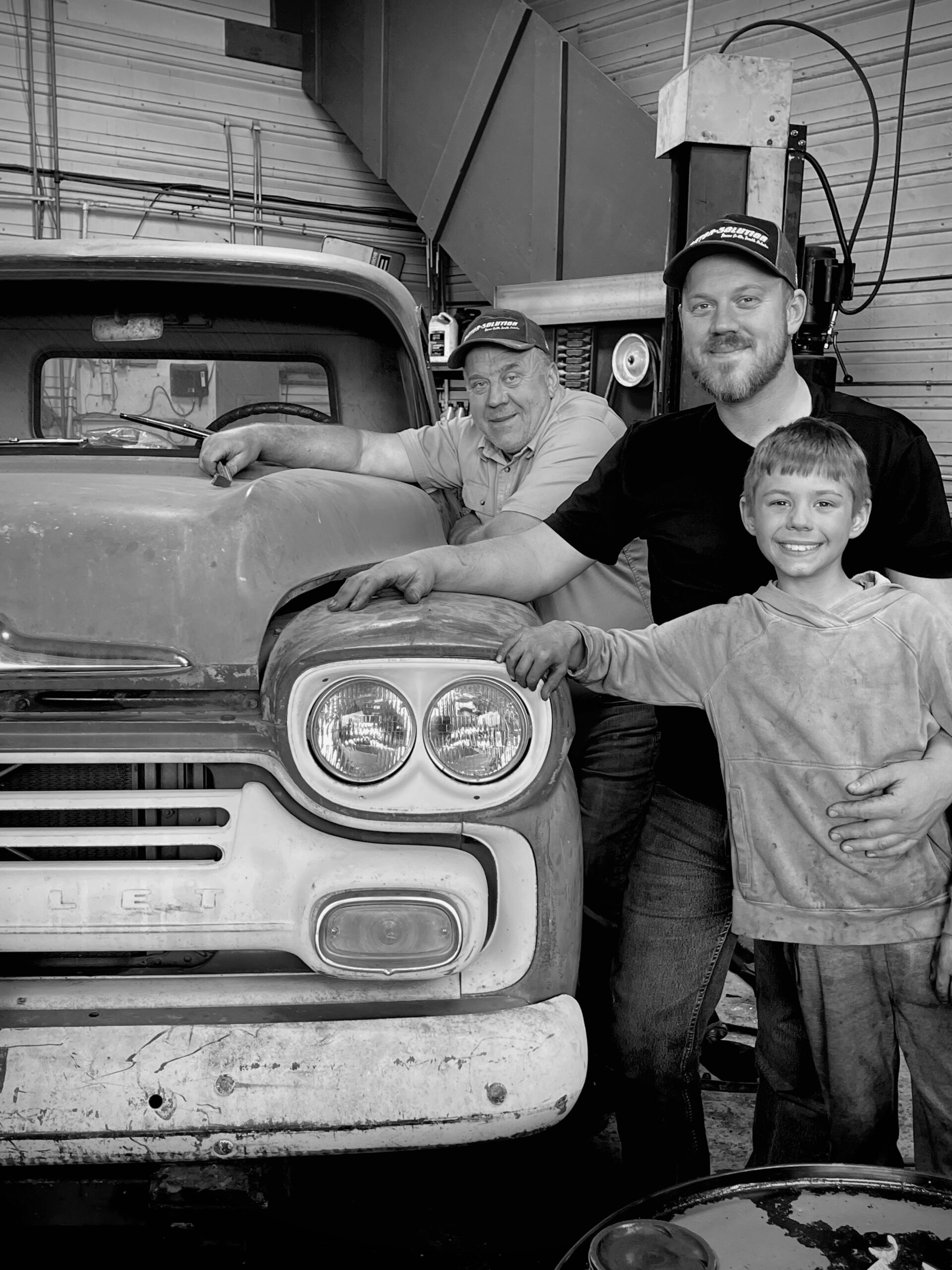 Family working on vintage truck at Motor Solution auto repair shop.