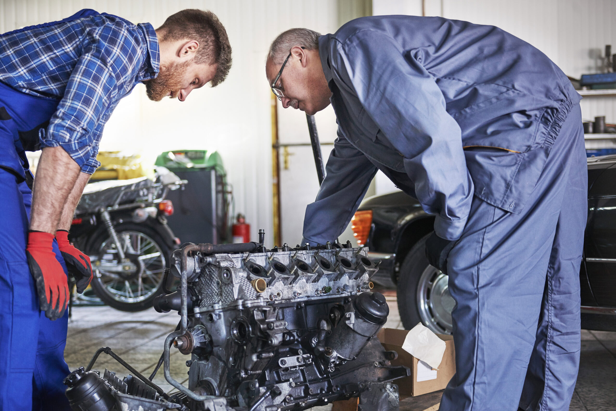 Engine repair specialists diagnosing a vehicle engine in a workshop.