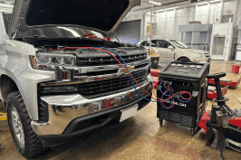 Technician repairing vehicle's air conditioning system with diagnostic equipment.