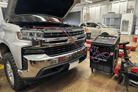 Auto repair technician performing vehicle air conditioning recharge.