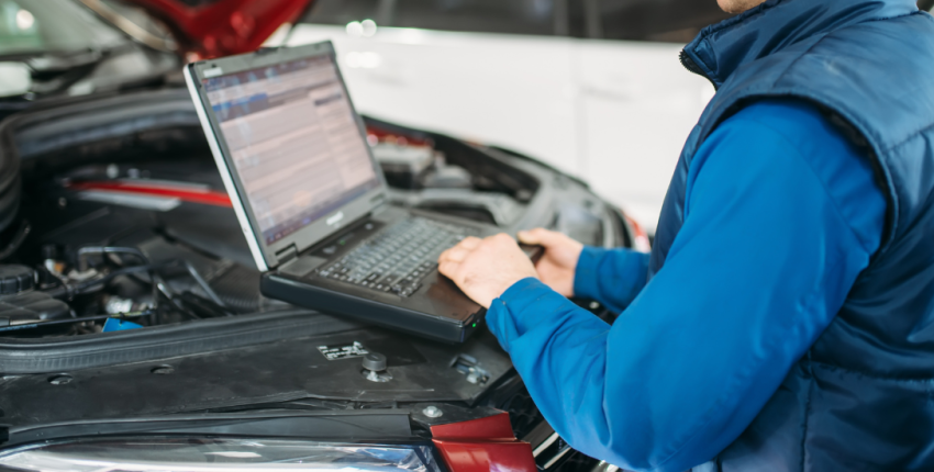 Engine repair technician diagnosing vehicle issues with a laptop under the hood.