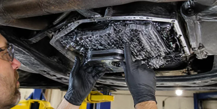 Mechanic inspecting the oil pan beneath a vehicle during repair.