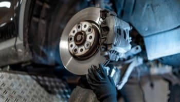 Technician inspecting car brake disc and caliper during repair.