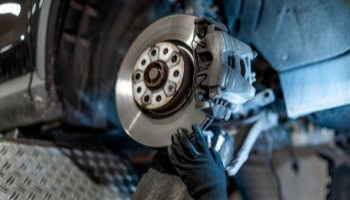 Technician inspecting a car's brake disc and caliper during repair.