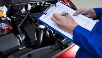 Technician inspecting car engine with clipboard at Nathan's Garage Ltd.