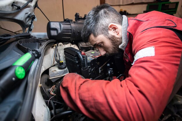 Auto mechanic inspecting car engine for seasonal maintenance.