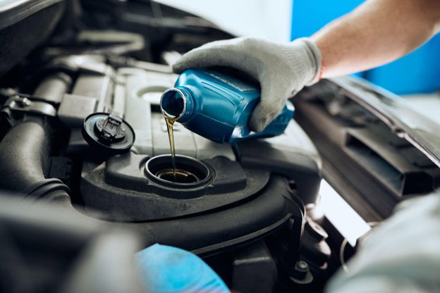 Auto mechanic pouring oil into a car engine during maintenance.