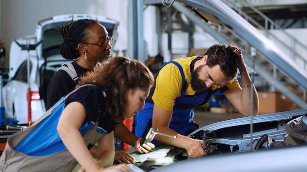 Team of technicians inspecting and repairing a damaged car using tools and inspection lamp