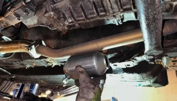 Mechanic performing oil change on vehicle underside at Noyzboyz Performance.
