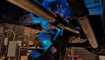 Technician inspecting vehicle underside during performance check at Noyzboyz.