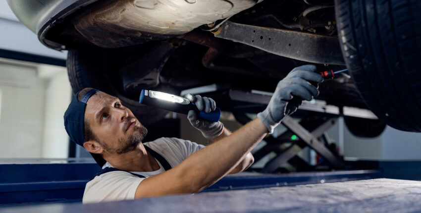 Technician performing an oil change on a car lifted on a hydraulic lift.