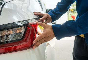 Auto technician inspecting car tail light for maintenance or repair.